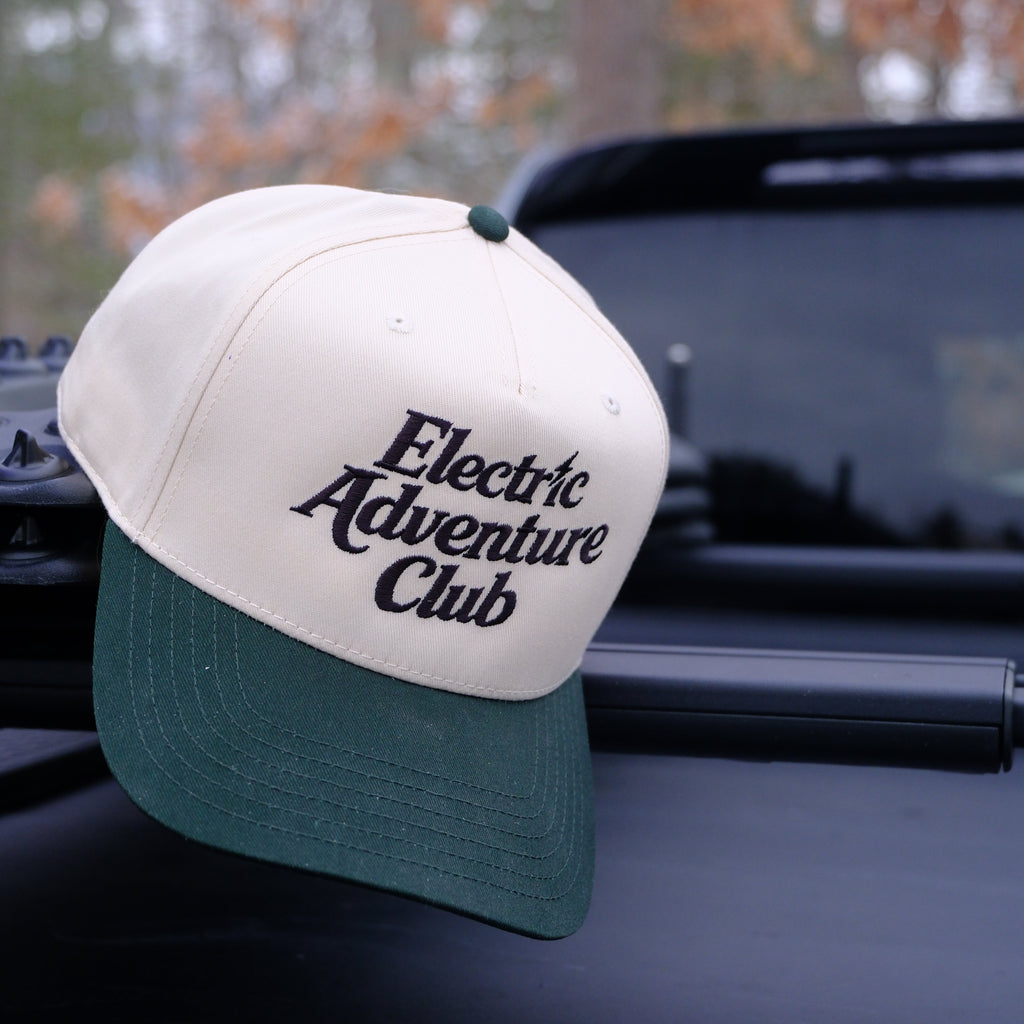 Cap with 'Electric Adventure Club' logo on a car window